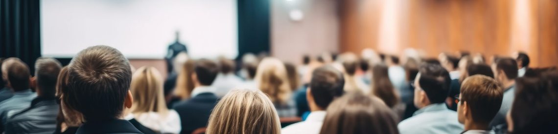 Rear view of people in audience at the conference hall, Speaker giving a talk in conference hall at business event.
